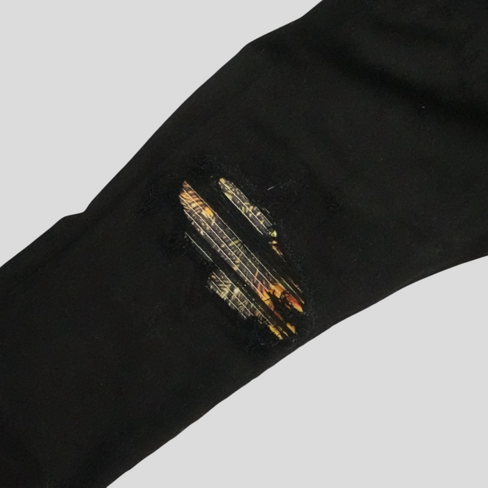 CLB XXIII Amiri black cotton jeans featuring a distressed knee detail with a vibrant sunset-patterned Aloha patch