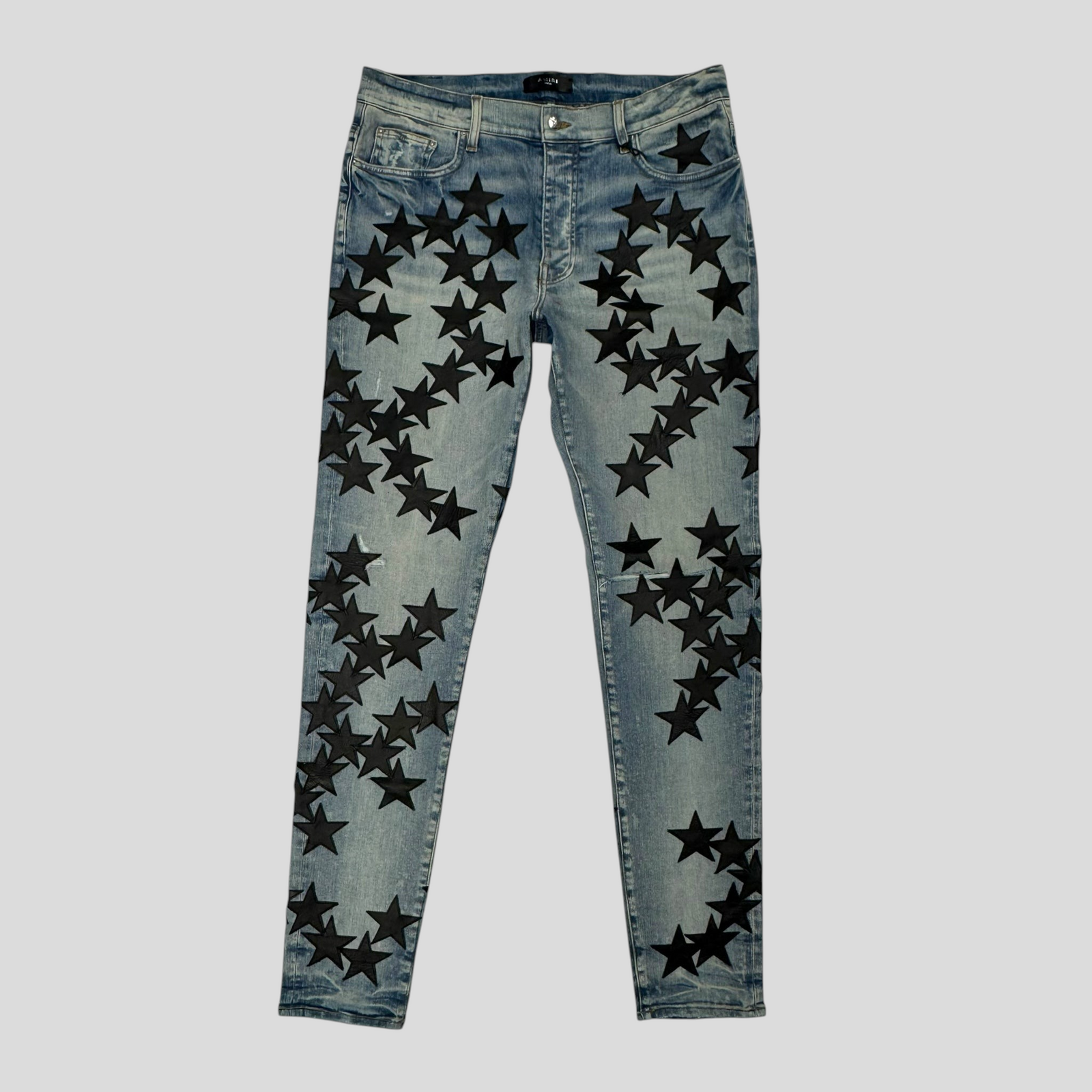 CLB XXIII Amiri Chemist star patch jeans in clay indigo denim with black star appliqués and distressed detailing.