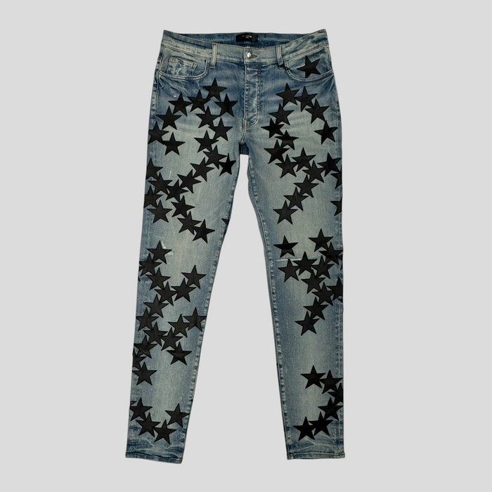 CLB XXIII Amiri Chemist star patch jeans in clay indigo denim with black star appliqués and distressed detailing.