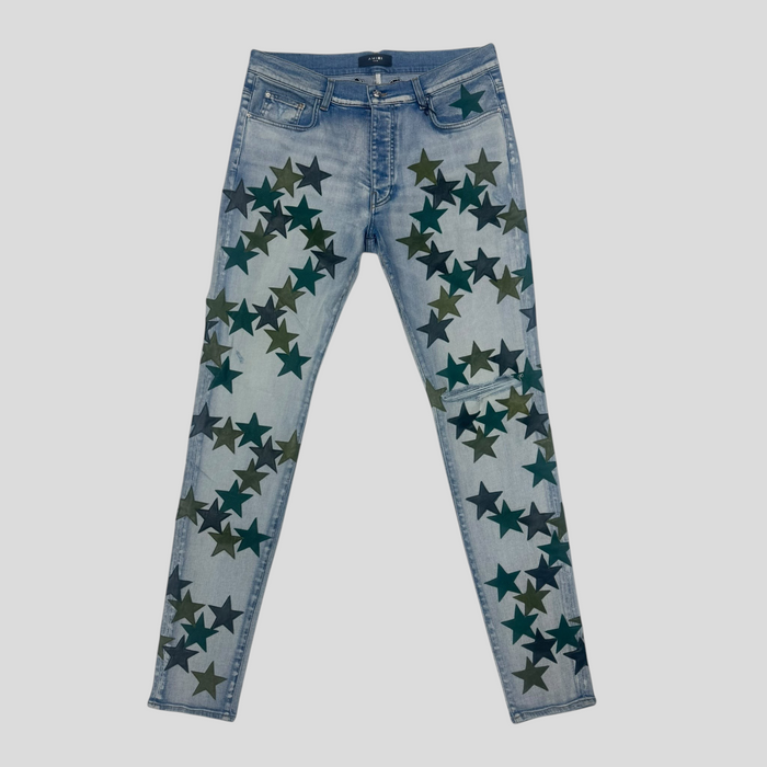 CLB XXIII Amiri Chemist light indigo denim jeans featuring dark green star patches and a slim fit design.