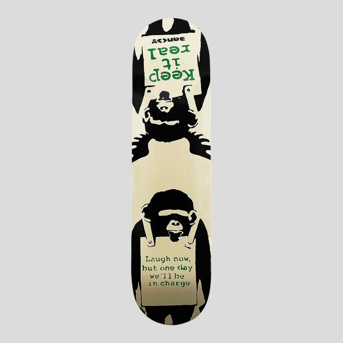 CLB XXIII Banksy Laugh Now skateboard deck featuring a black and white monkey graphic with green text on a cream base.