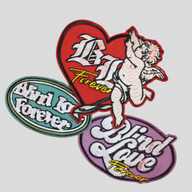 CLB XXIII Blind Love patchwork set featuring red heart, teal oval, and purple oval embroidered patches with cherub